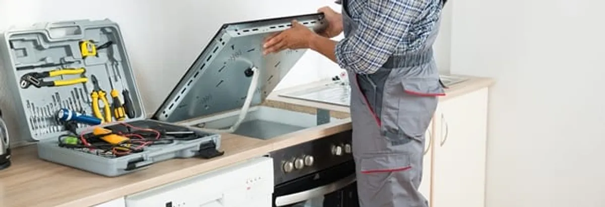 Cooktop repair technician lifting a built-in stovetop for service in Spokane, WA