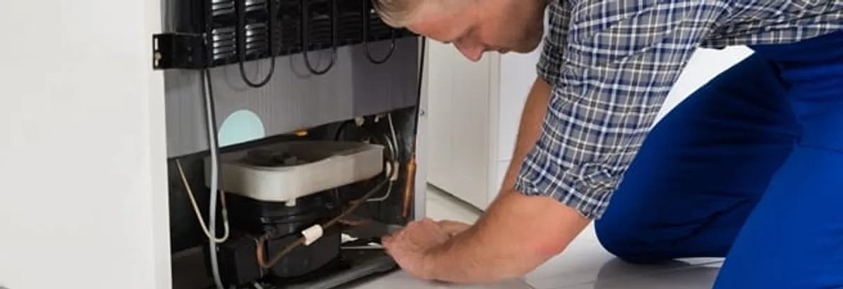 Refrigerator repair technician servicing the compressor and condenser area in Spokane, WA